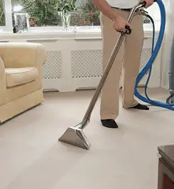 Professional carpet cleaner using a hot-water extraction wand and hose machine in a living room in Irvine, CA.