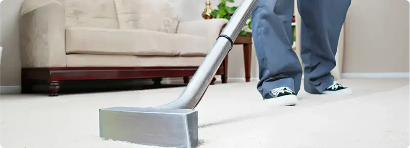 Carpet cleaning technician using a hot-water extraction wand on a light-colored carpet in a living room, Irvine, CA.