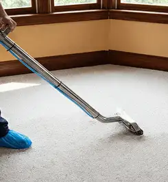 Steam carpet cleaning technician using a hot-water extraction wand on a residential carpet, wearing blue protective shoe covers Irvine, CA.