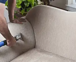 Professional upholstery cleaner deep-cleaning a fabric sofa with a handheld extraction tool and hose in Irvine, CA.